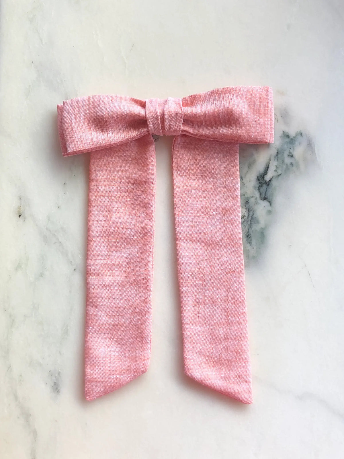 Broochella Men's Sofia peach linen bow brooch, a handmade designer statement accessory with an oversized bow and elegant long ribbon tails, photographed on white marble.