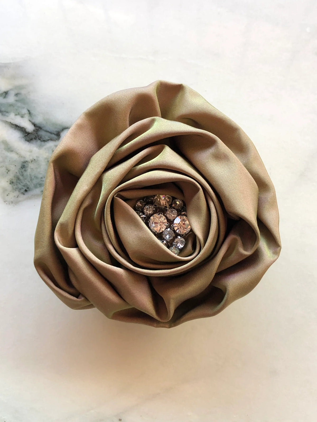 Broochella Sofia Rose Bloom Brooch featuring sculptural bronze silk petals with a sparkling crystal centre, photographed on a white marble background.