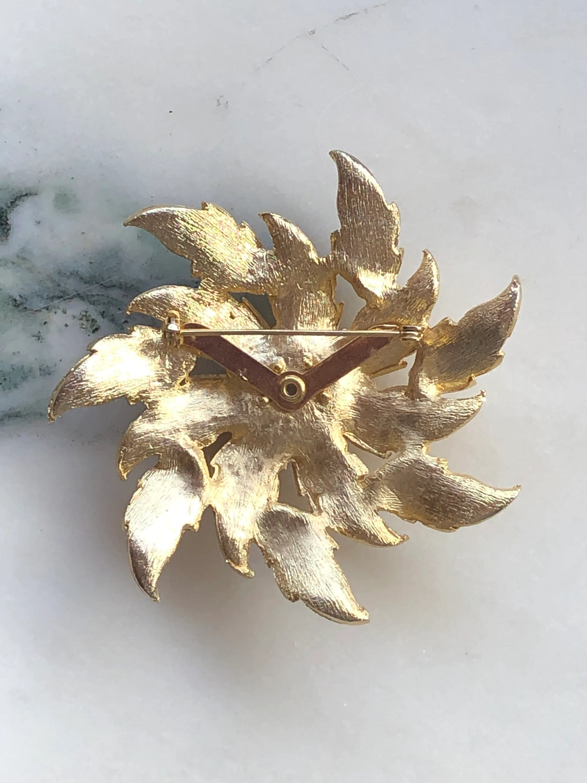 Broochella Sole d’Oro Vintage Brooch back view showing the textured gold-tone leaf construction and traditional pin fastening, photographed on white marble with natural grey-green veining.