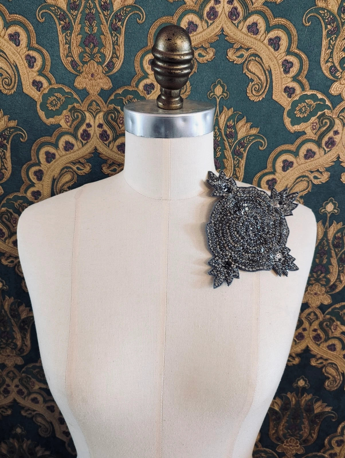 Broochella Stella hand beaded silver statement brooch Pictured on a mannequin. The background is green and gold damask wallpaper