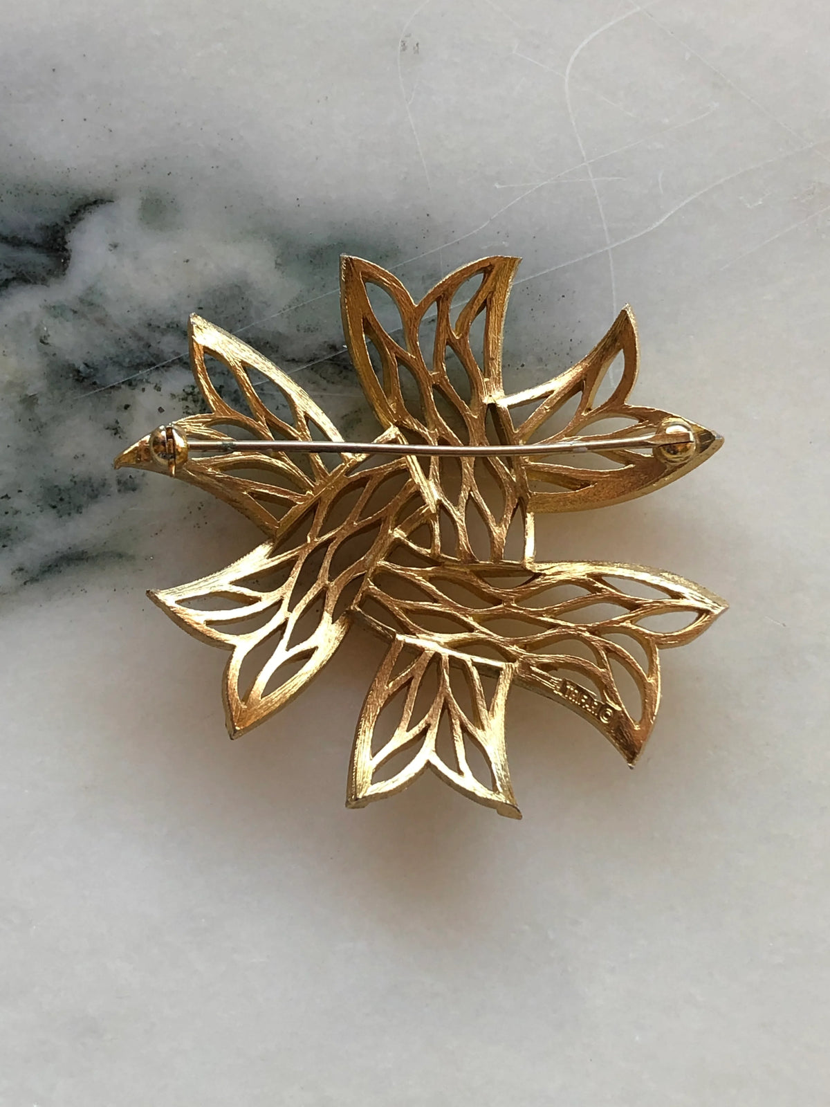 Broochella Stella Dorata Trifari Vintage Brooch Pin back view showing the openwork gold-tone construction, Trifari signature and pin fastening, photographed on white marble with soft grey-green veining.