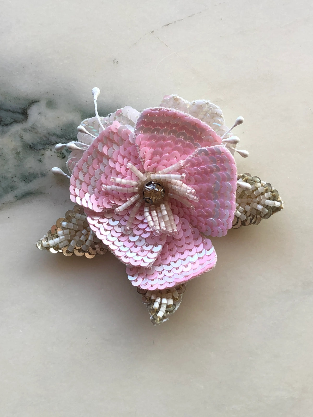 Broochella Men's Tesorino Sequinned Flower Brooch Pin with layered pink sequinned petals, ivory beading and crystal details, photographed on a white marble background with soft grey veining.
