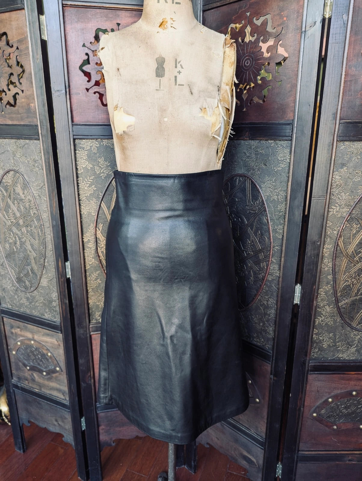 Scanlan Theodore Black Leather Skirt – AU 8 / US 4. Pictured on a mannequin. The background is an ornate dark wood screen. 