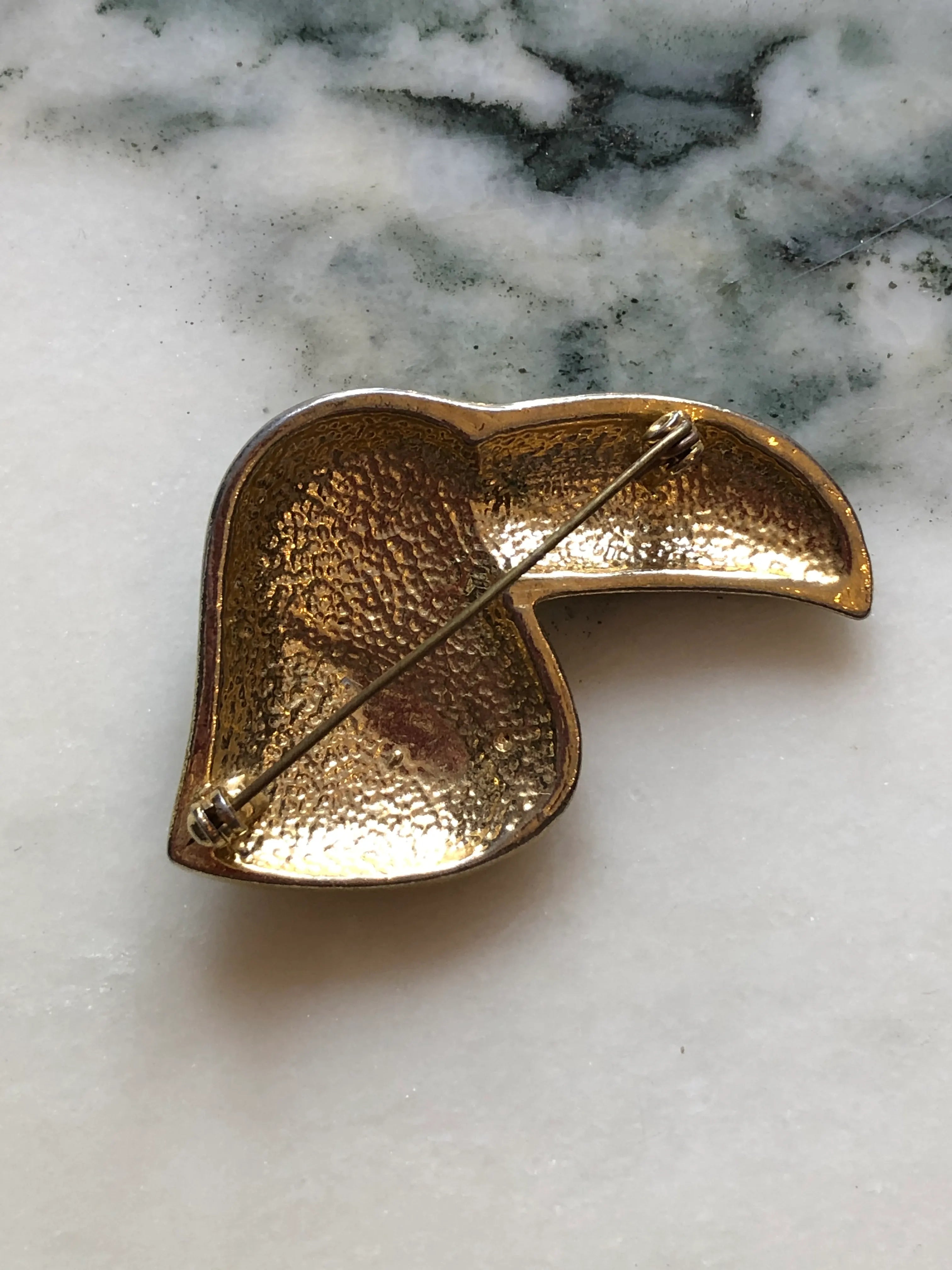 The back view of vintage Broochella Toucano Nero  toucan head brooch featuring black enamel, gold-tone metal, and clear rhinestones on a light marble surface.