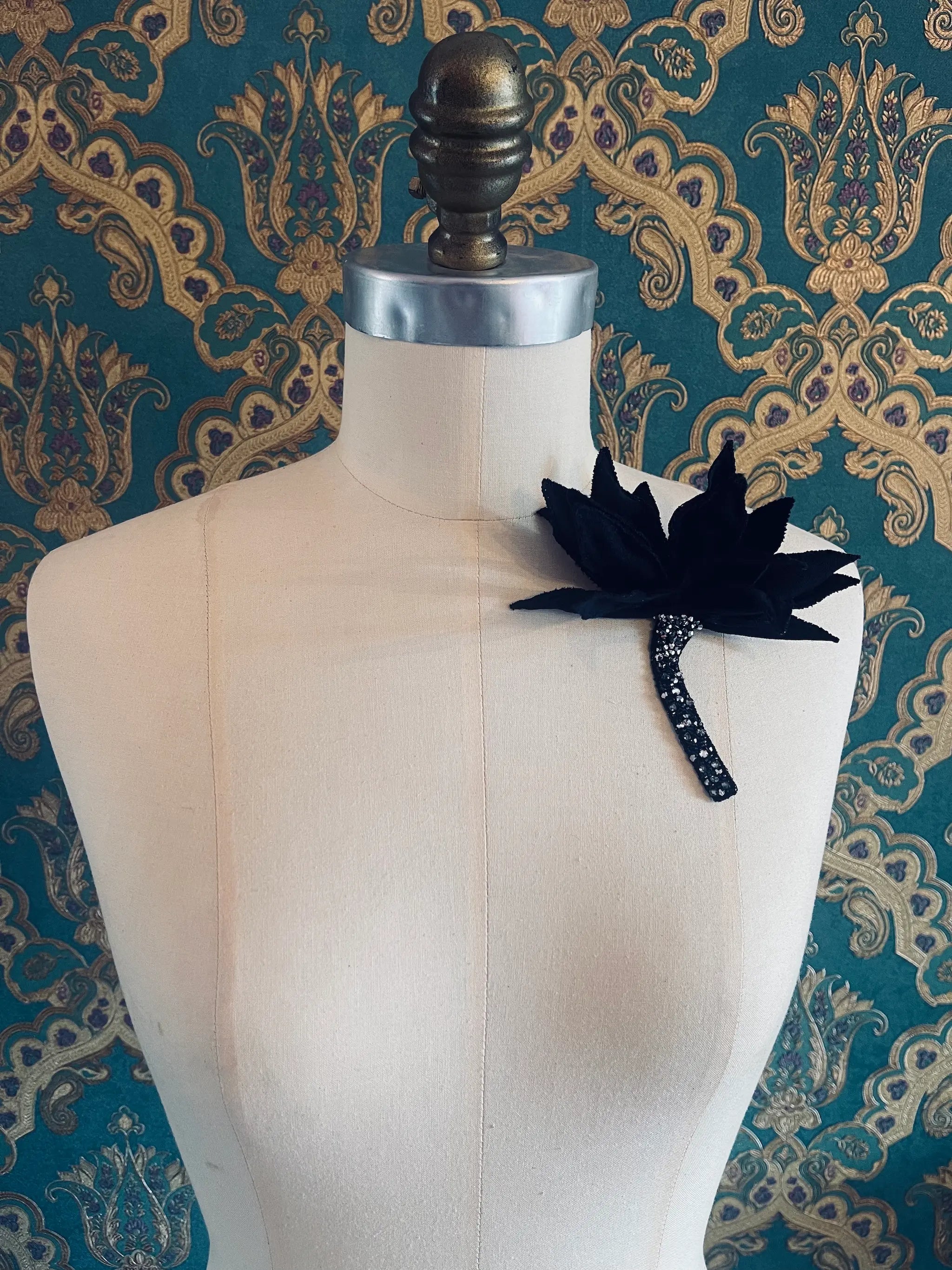 Broochella Tulipano handmade black and crystal flower brooch. Pictured on a mannequin. The background is green and gold damask wallpaper