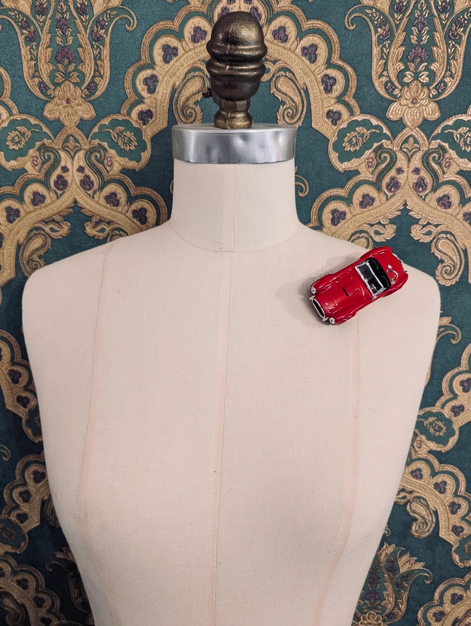 Broochella  scuderia d'oro rosso roadster 427 red, vintage formula one racing car brooch. Pinned on a mannequin. The background is green and gold damask wallpaper. 