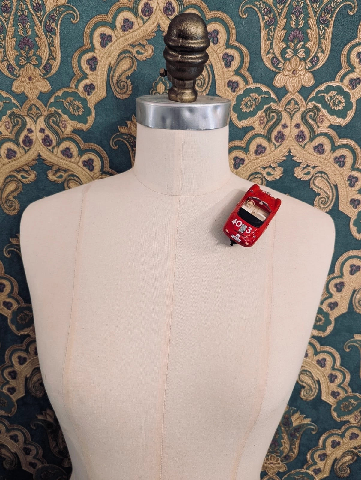 Broochella  scuderia d'oro  rosso mille 403 red vintage formula one racing car brooch. Pinned on a mannequin. The background is green and gold damask wallpaper. 