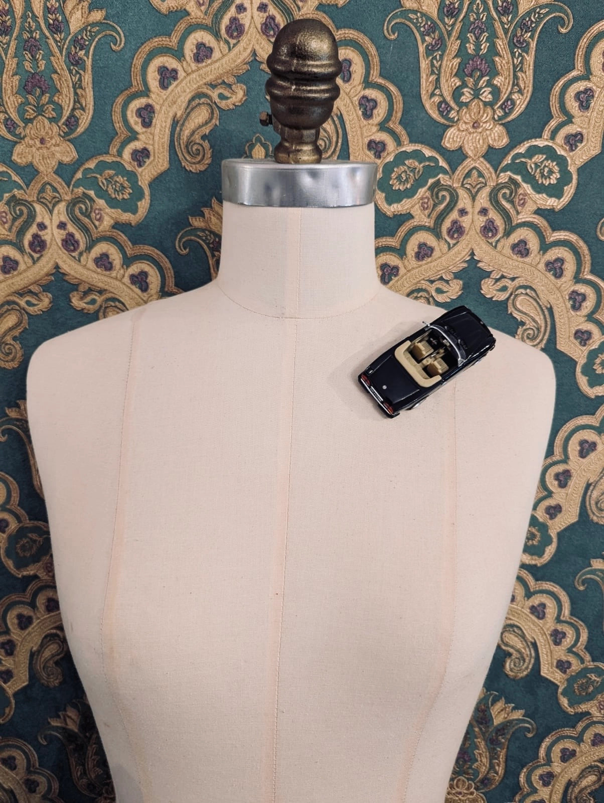 Broochella  scuderia d'oro nero riviera 84 black, vintage formula one racing car brooch. Pinned on a mannequin. The background is green and gold damask wallpaper. 