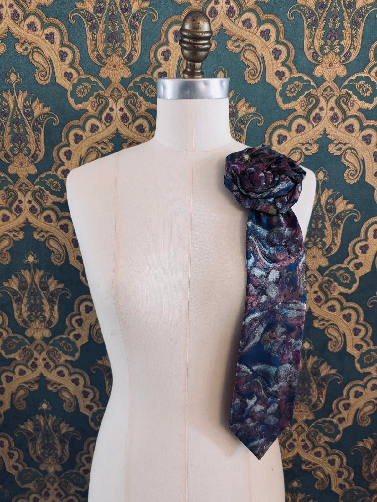 Broochella Saverio vintage up-cycled vintage handcrafted rosette tie in blue and pink. Pinned on a mannequin. The background is green and gold damask wallpaper