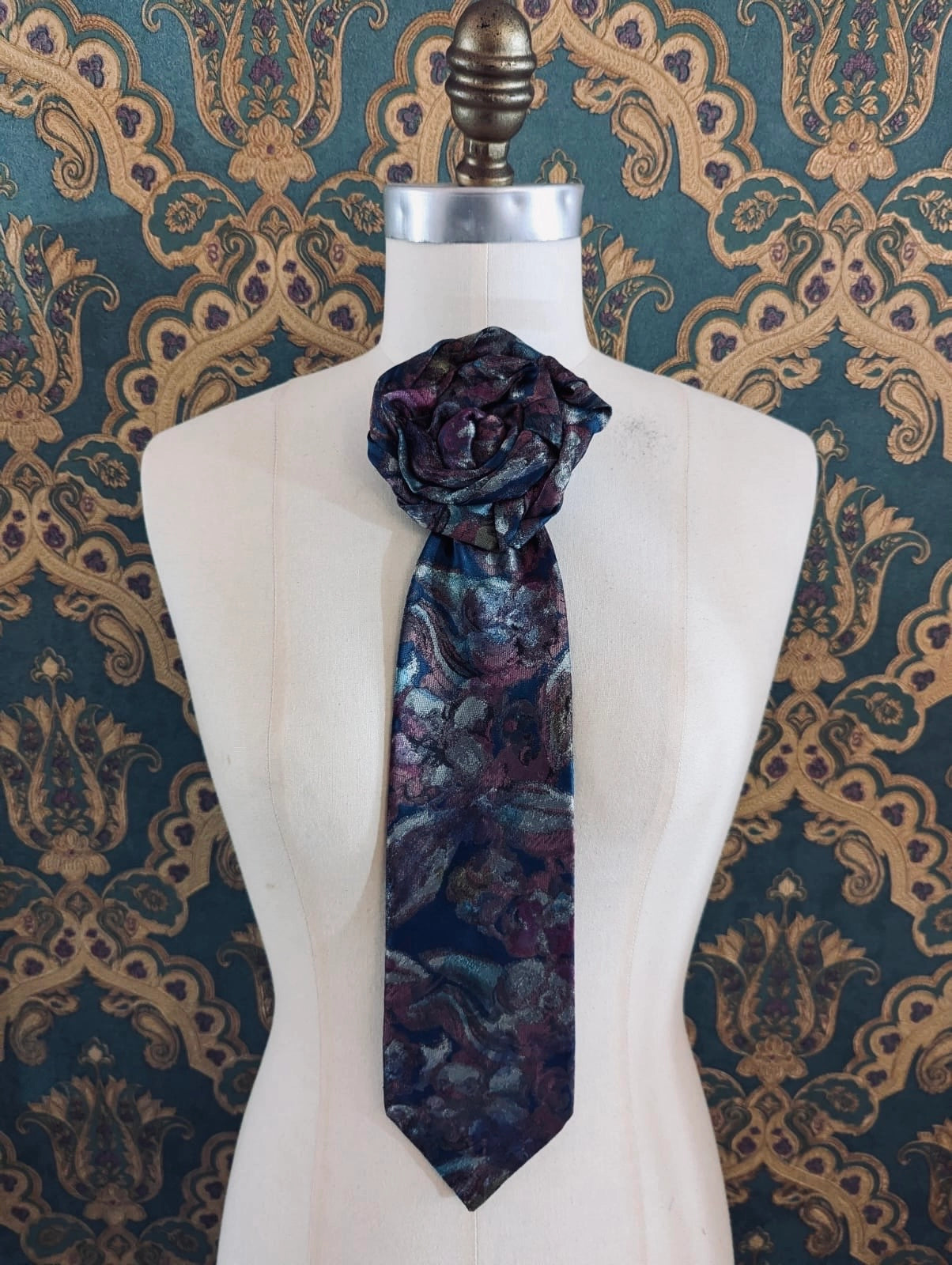 Broochella Saverio vintage up-cycled vintage handcrafted rosette tie in blue and pink. Pinned on a mannequin. The background is green and gold damask wallpaper