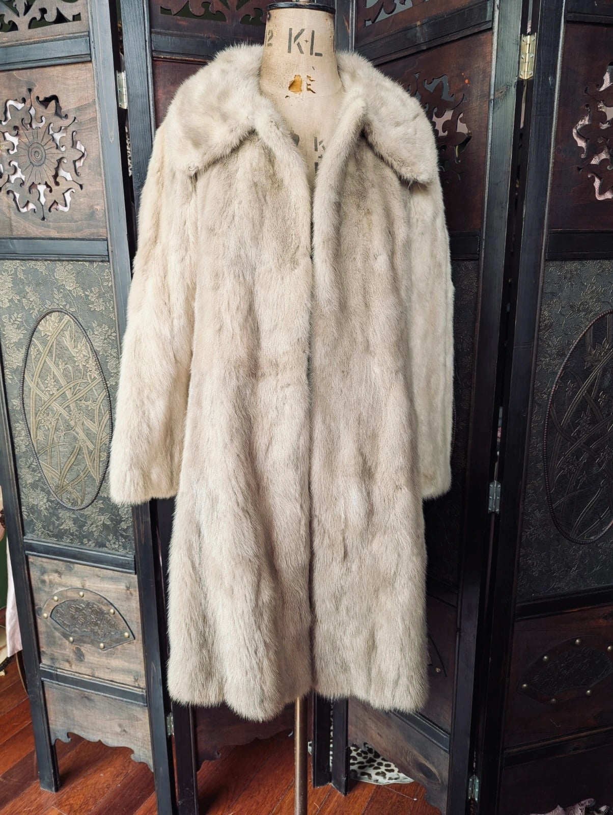 A Broochella  long vintage cream-colored fur coat displayed on a mannequin torso in front of a dark wooden folding screen.
