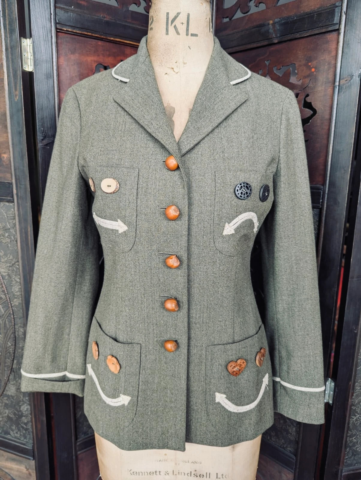 Broochella authentic designer Moschino Cheap and Chic Vintage green jacket with brown button faces on a mannequin against a dark background. 