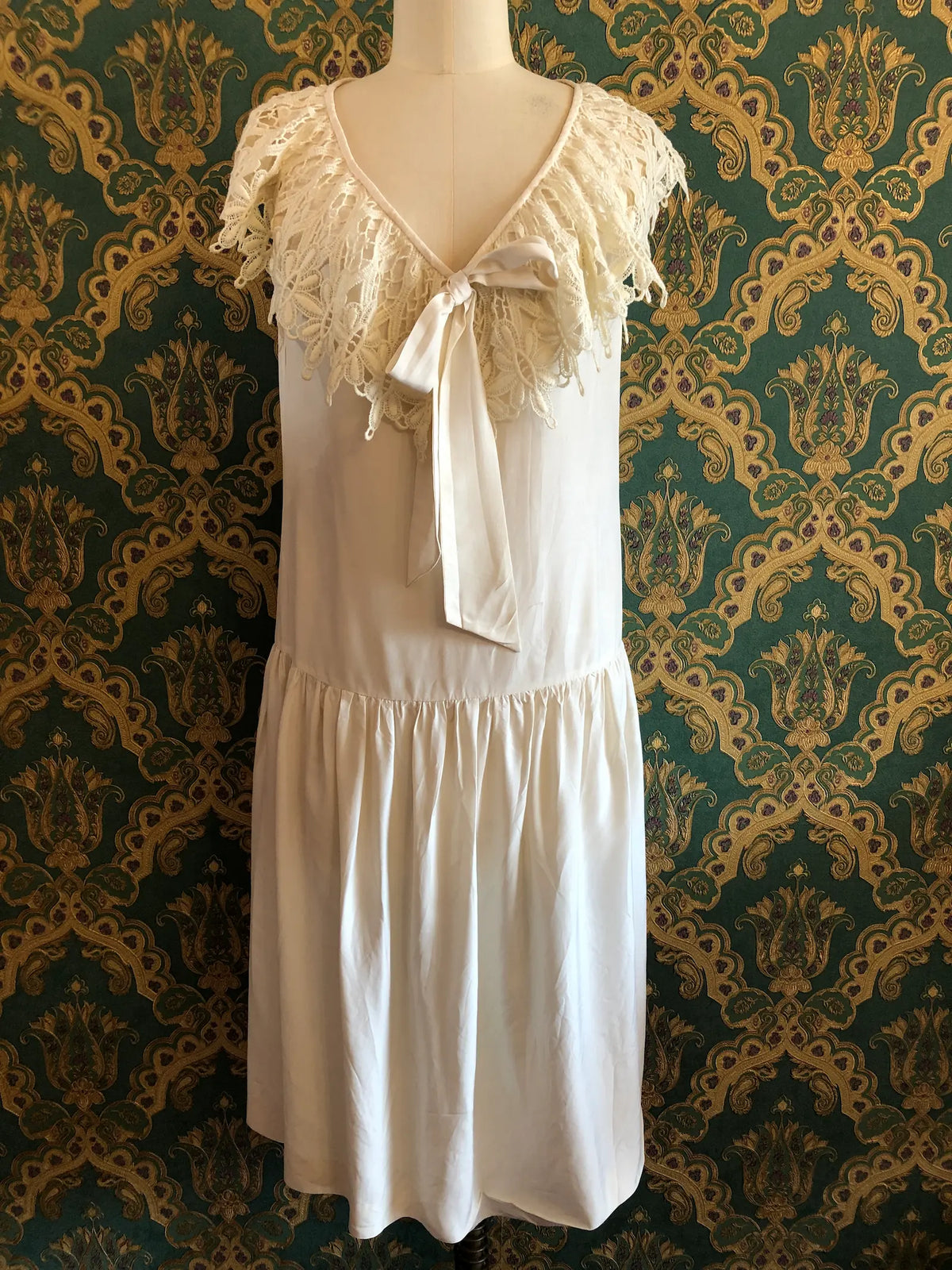 Broochella vintage Ninette ivory silk maxi dress with an ornate lace cape collar, deep V-neckline and satin bow, labelled vintage AU 12 and approximately modern AU 8. Pictured on a mannequin against green and gold damask wallpaper.