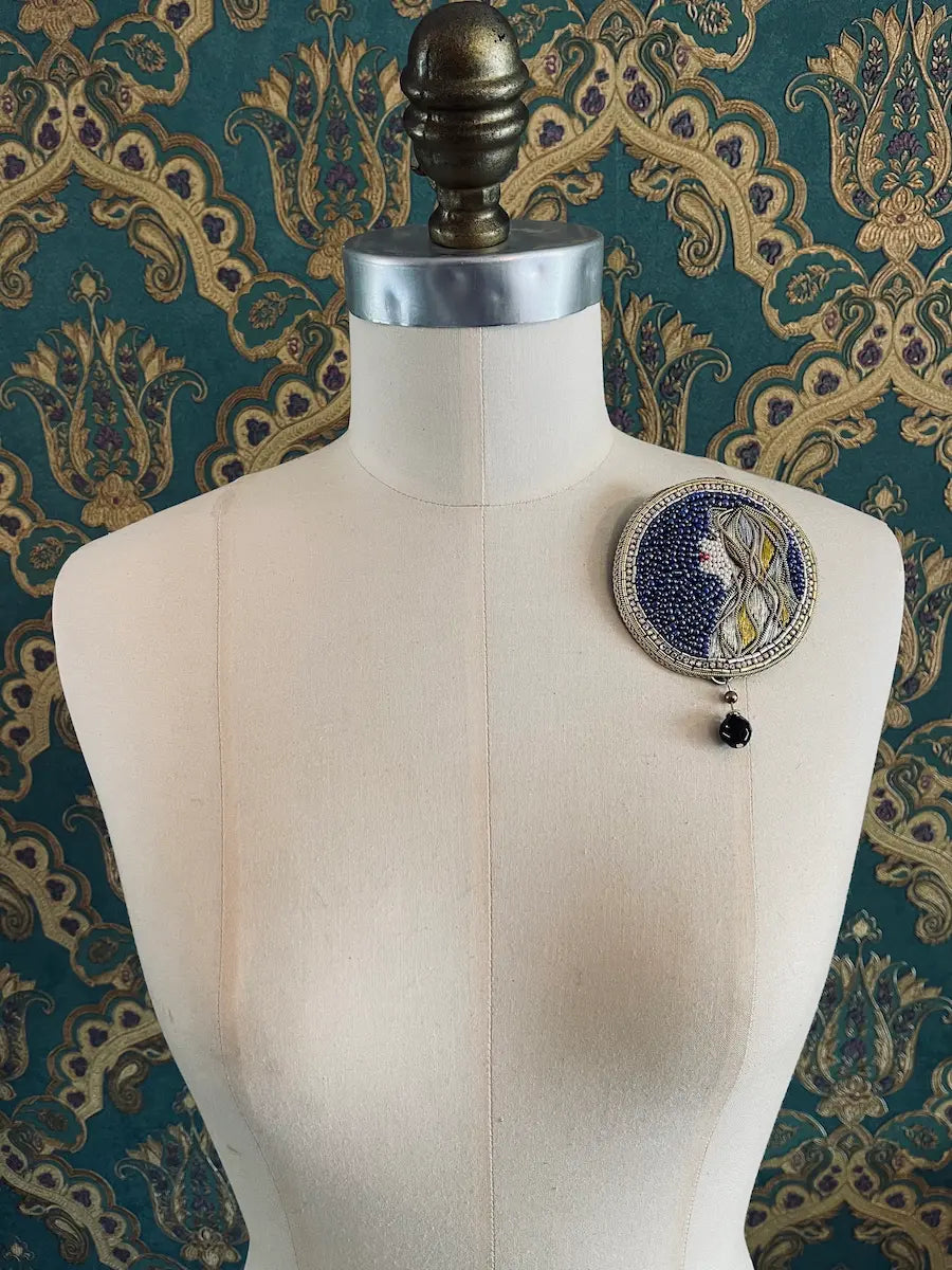 Broochella virgo zodiac hand beaded designer brooch. Pictured on a mannequin. The background is green and gold damask wallpaper