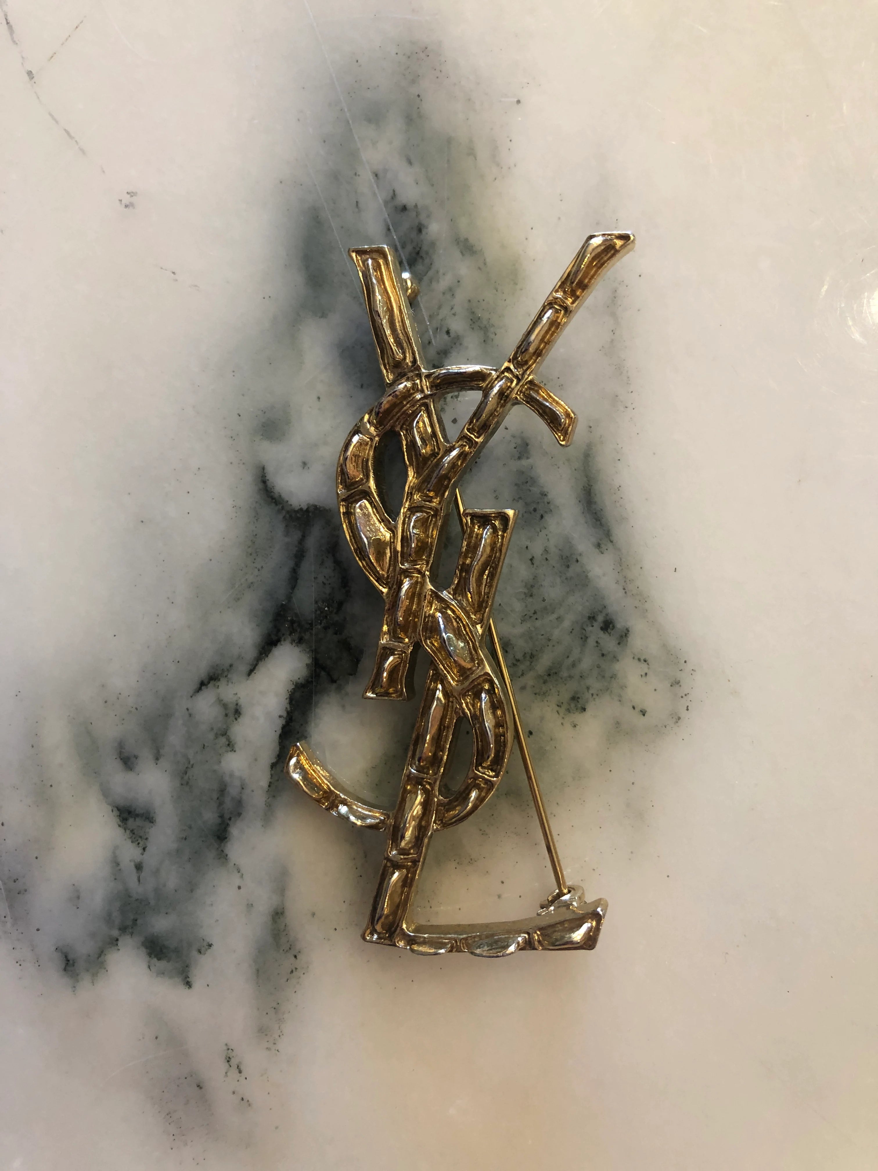 Broochella Yves Saint Laurent costume, gold tone logo brooch. the background is white marble