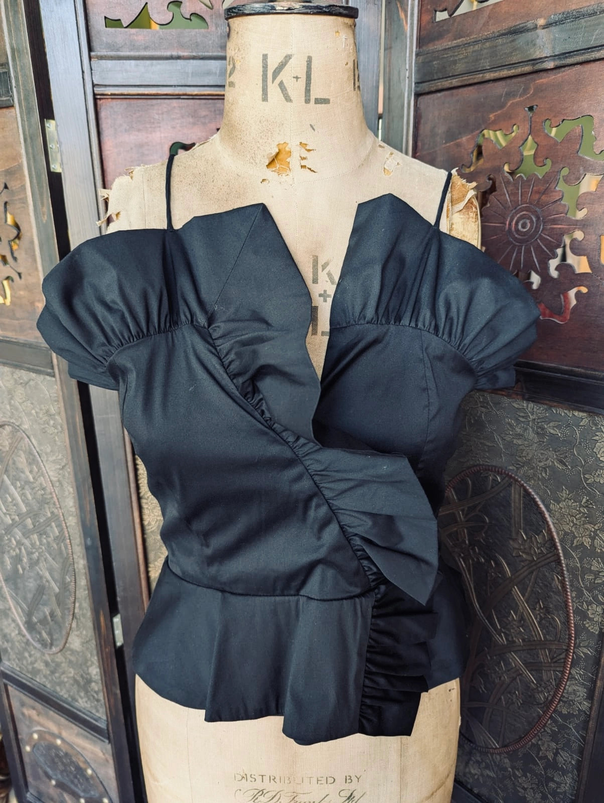 Broochella Zara black ruffle peplum cami top in black. Pictured on a mannequin. The background is an ornate dark wood room divider