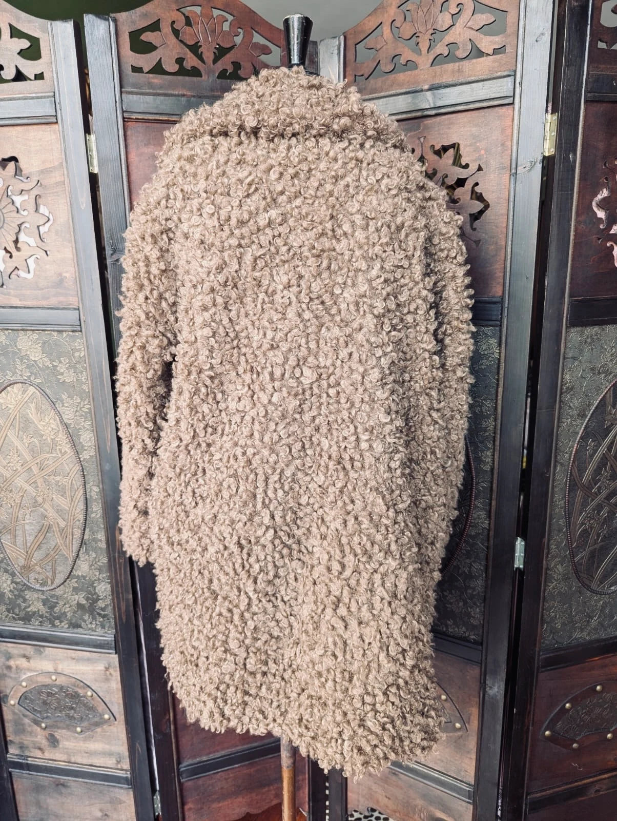 Broochella Zara Brown Teddy Faux fur coat. It is pictured on a vintage mannequin The background is an ornate, vintage, dark wood room divider.