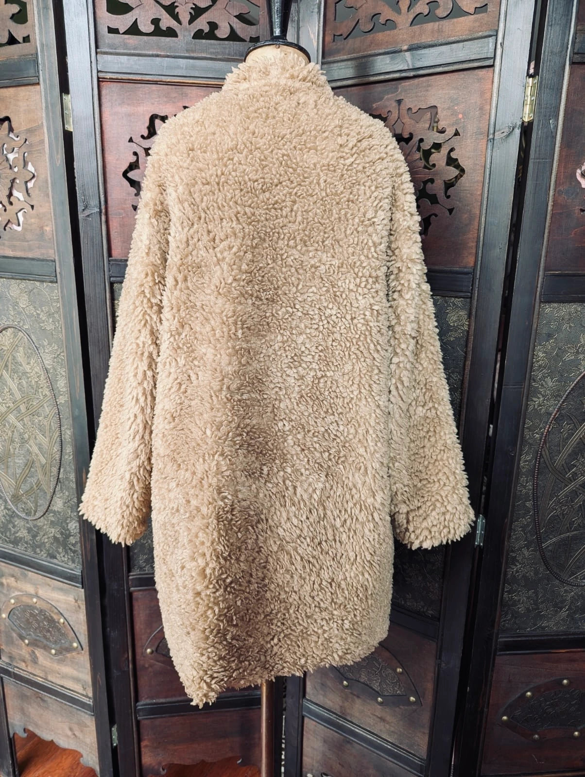 Broochella The Stylist's Closet Zara brown teddy fur coat from the back. It is pictured on a vintage mannequin. The background is an ornate, vintage, dark wood room divider. 