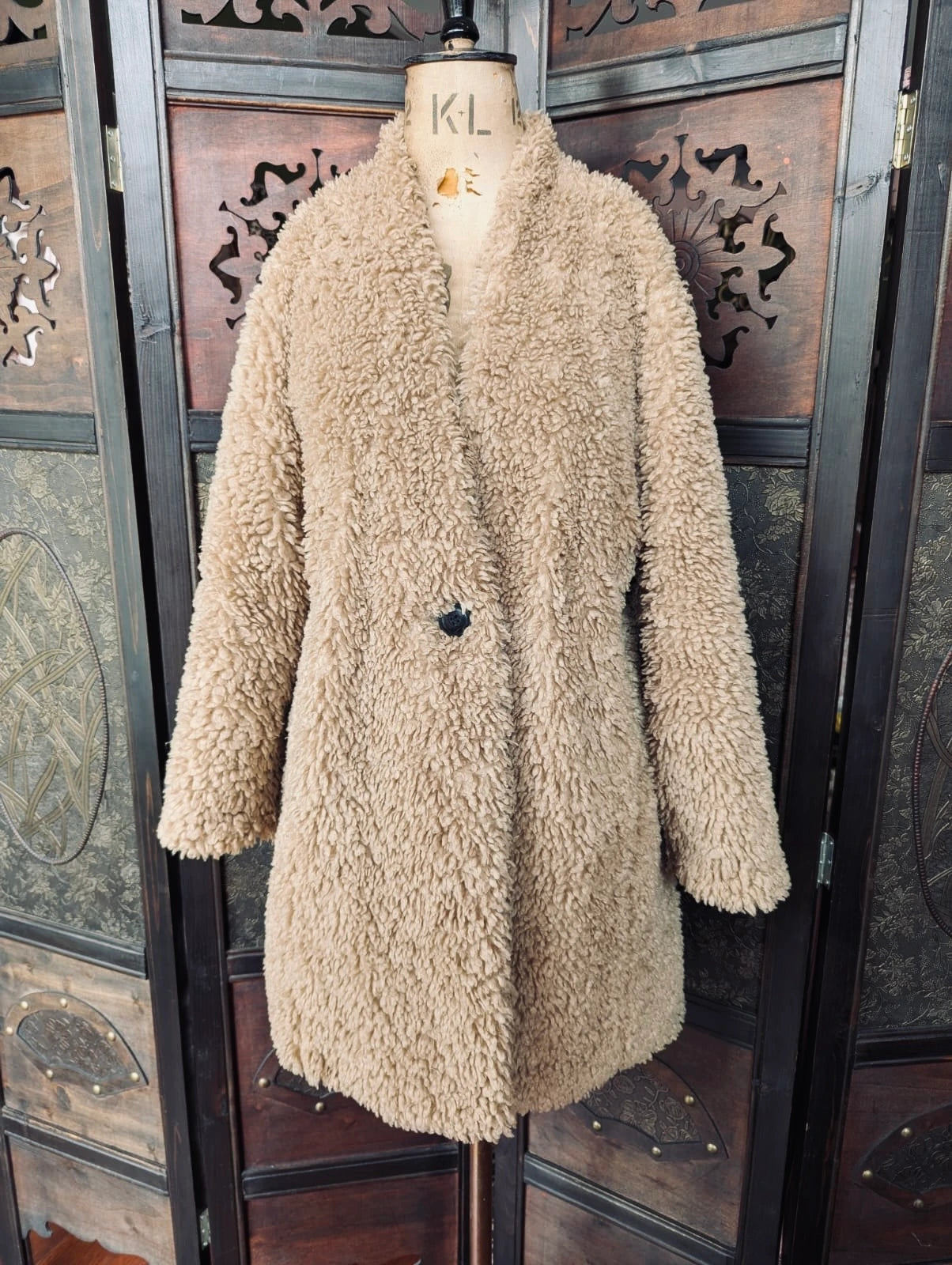 Broochella The Stylist's Closet Zara brown teddy fur coat. It is pictured on a vintage mannequin. The background is an ornate, vintage, dark wood room divider. 