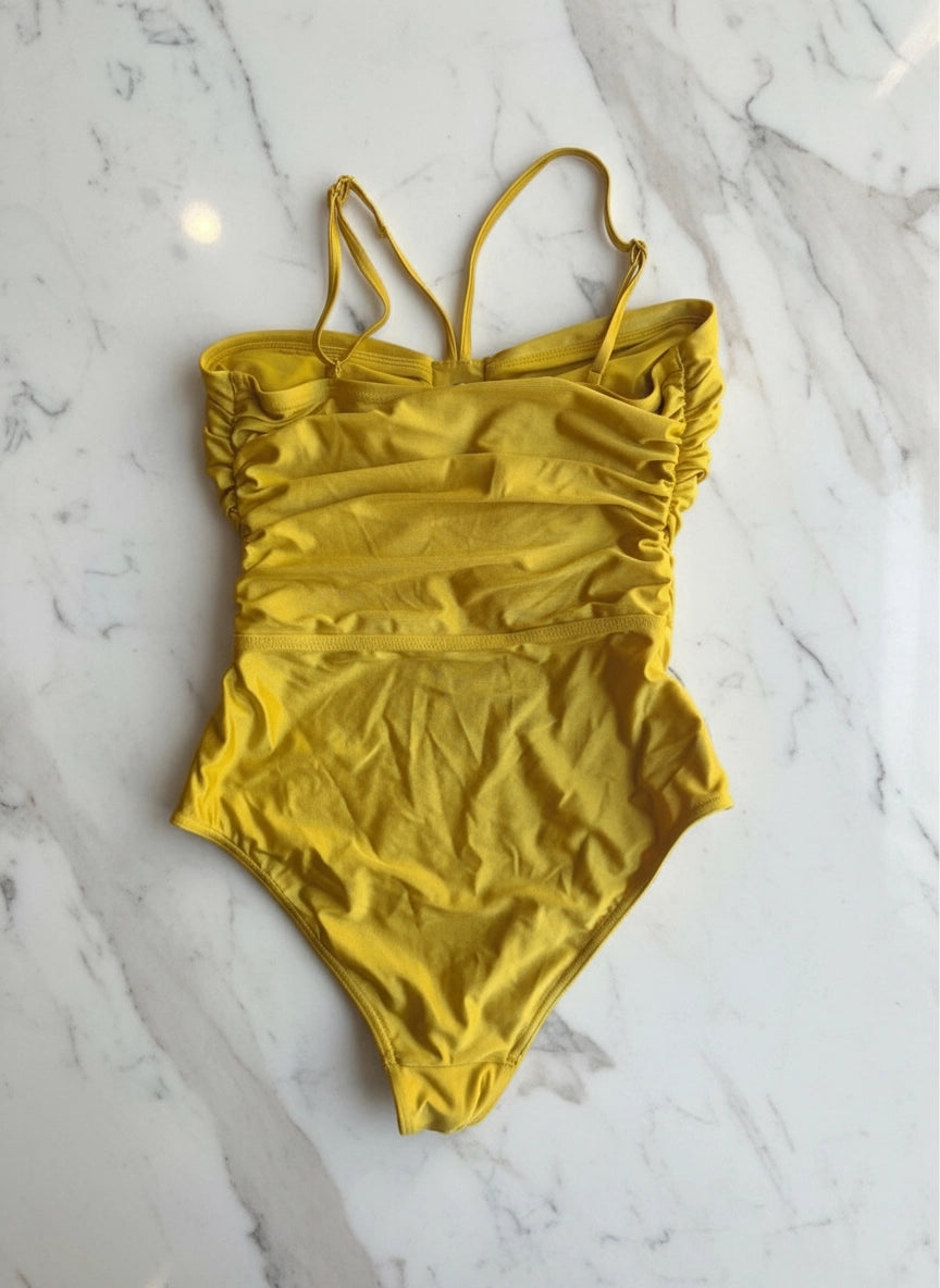 A Broochella Zimmerman mustard yellow one-piece swimsuit with a ruched corset-style bodice and thin shoulder straps back view, laid flat on a white marble surface.