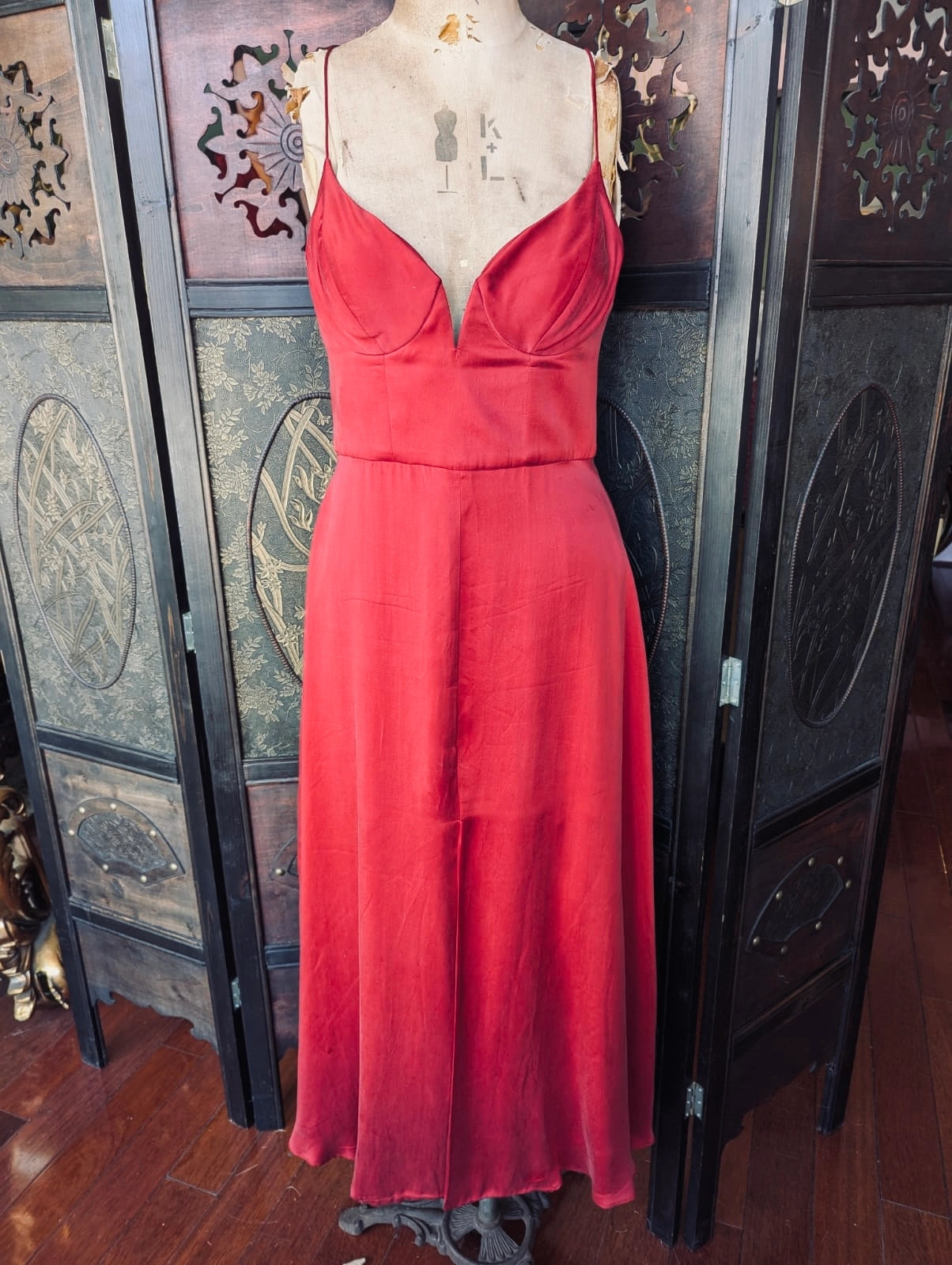 Broochella Zimmerman designer red silk midi dress. It is pictured on a mannequin. The background is an ornate, dark wood room divider
